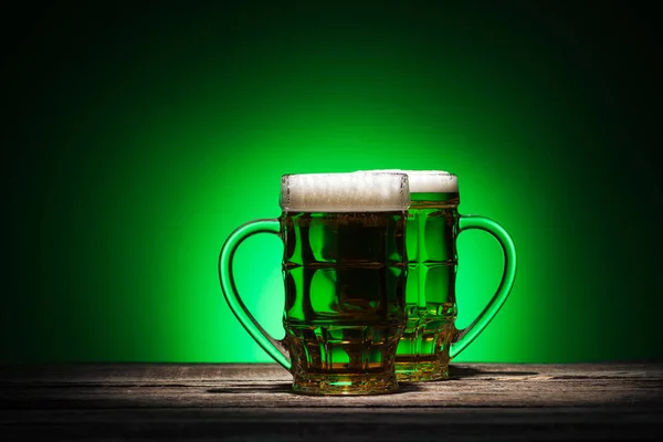 Copos de cerveja verde em pé sobre mesa de madeira sobre fundo verde — Fotografia de Stock