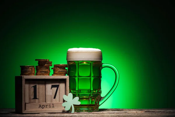 Verre de ale irlandaise verte près de pièces d'or et calendrier cube sur fond vert — Photo de stock