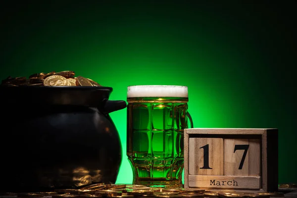 Vidro de cerveja irlandesa perto de moedas de ouro no calendário pote e cubo no fundo verde — Fotografia de Stock