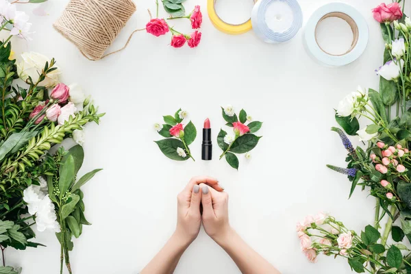 Vista ritagliata di mani femminili, boutonnieres e rossetto circondato da fiori su sfondo bianco — Foto stock