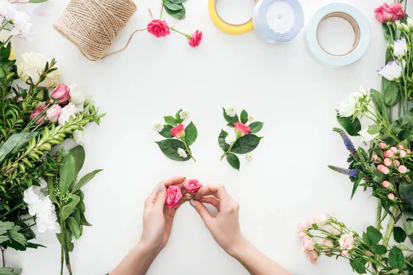 Vista ritagliata di mani femminili che tengono boccioli di rosa su boutonnieres e circondato da fiori su sfondo bianco — Foto stock