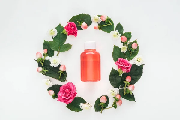 Top view of circular composition with green leaves, flowers and bottle with orange lotion isolated on white — Stock Photo