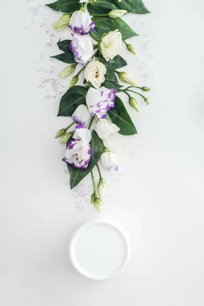 Верхний вид композиции с фиолетовой и белой эустомой, крем красоты в бутылке на белом фоне — стоковое фото