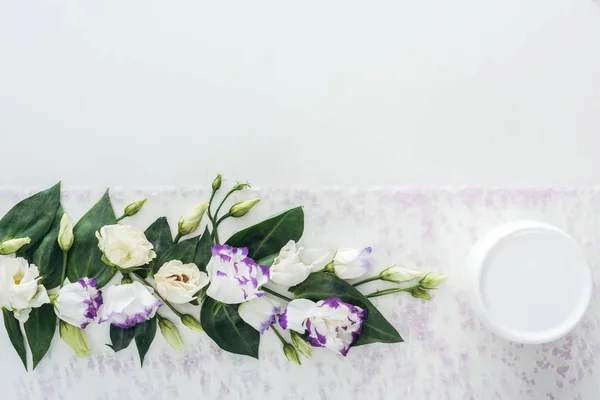 Vista dall'alto della composizione con eustoma viola e bianco, crema di bellezza in bottiglia su sfondo bianco strutturato — Foto stock