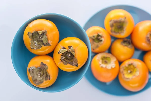 Selective focus of whole and sweet persimmons on blue glass plates — Stock Photo
