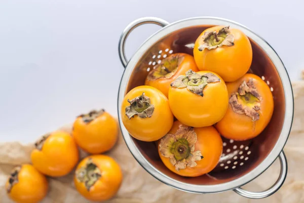 Foco seletivo de caquis de laranja inteiros maduros em escorredor — Fotografia de Stock