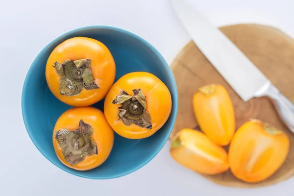 Selective focus of persimmons on blue plate and slices on cutting board — Stock Photo