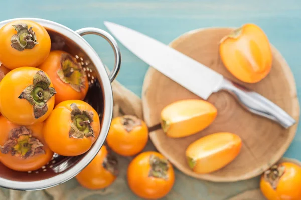 Foyer sélectif de kaki orange en passoire et tranches sur planche à découper avec couteau — Photo de stock