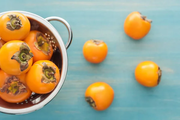 Foco selectivo de jugosos caquis de naranja en colador sobre fondo azul — Stock Photo