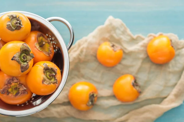 Selective focus of whole persimmons in colander on blue background — Stock Photo