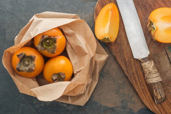 Top view of whole persimmons in paper packet and sliced on cutting board — Stock Photo