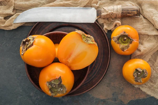 Top view of cut and whole persimmons in black plates with knife — Stock Photo