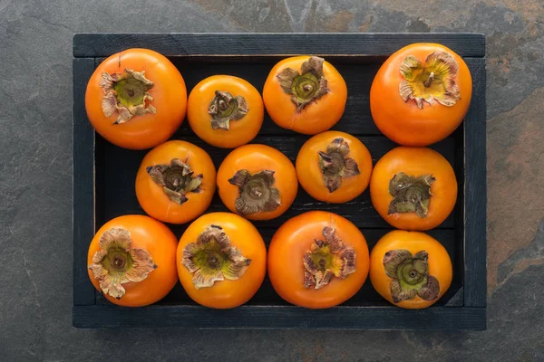 Vue de dessus des kaki orange et entiers dans une boîte en bois — Photo de stock