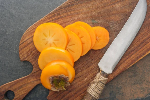 Top view of persimmons slices on cutting board with knife — Stock Photo