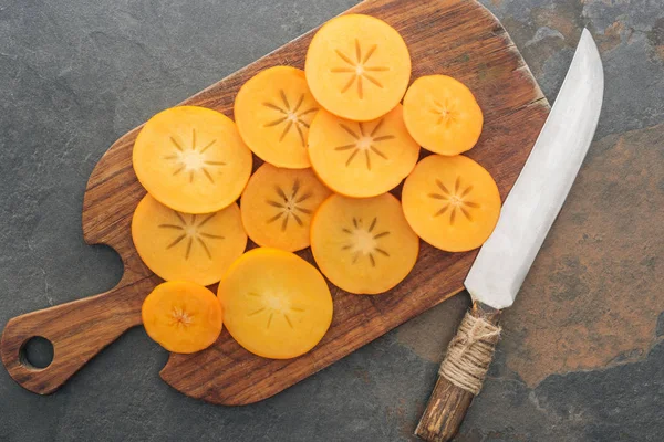 Vue de dessus de tranches de kaki orange sur planche à découper avec couteau — Photo de stock