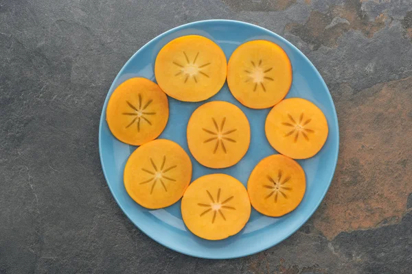 Vue de dessus de kaki orange tranché sur plaque bleue — Photo de stock