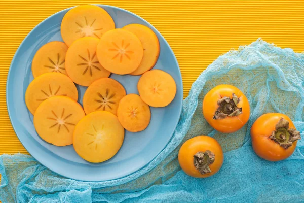Vista superior de rebanadas de caquis naranjas en placa azul - foto de stock