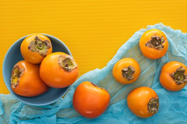 Вид сверху на всю апельсиновую хурму на голубой тарелке и ткани — стоковое фото