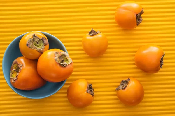 Top view of orange persimmons on blue plate on yellow background — Stock Photo