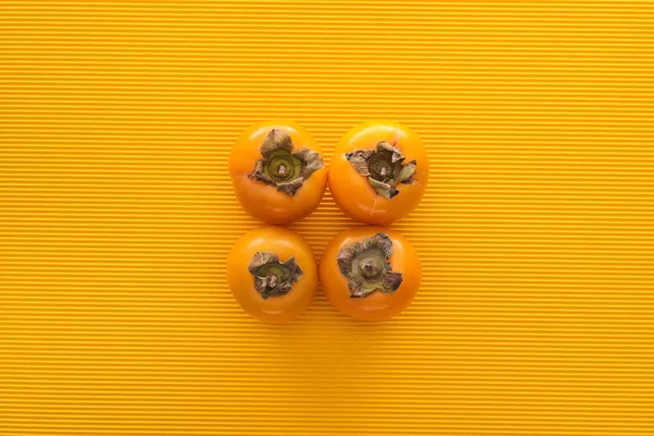 Вид сверху на цельную и оранжевую хурму на желтом фоне — стоковое фото