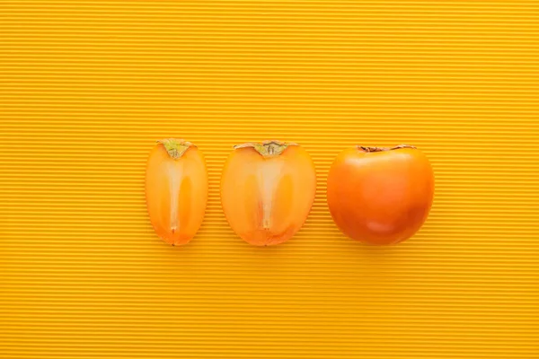 Top view of cut and whole persimmons on yellow background — Stock Photo