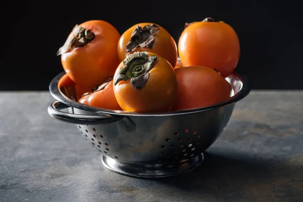 Orange and whole persimmons in colander isolated on black — Stock Photo