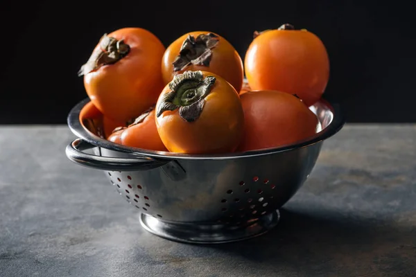 Laranja e caquis inteiros em escorredor isolado em preto — Fotografia de Stock