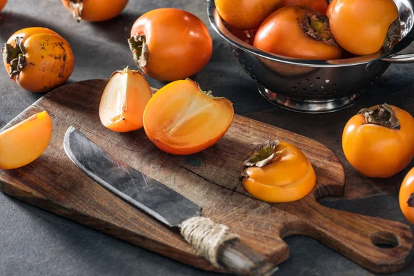 Sliced and whole orange persimmons on cutting board and in colander — Stock Photo