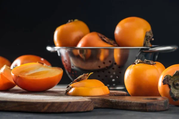 Selective focus of orange persimmons on cutting board and in colander — Stock Photo