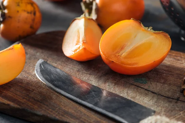 Caquis anaranjados y cortados en rodajas sobre tabla de cortar con cuchillo - foto de stock