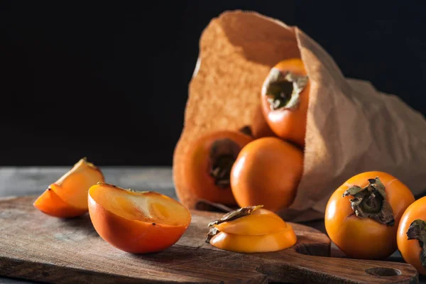 Selective focus of orange persimmons in paper packet and in cutting board — Stock Photo