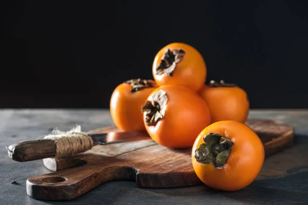 Kaki orange sur planche à découper avec couteau isolé sur noir — Photo de stock