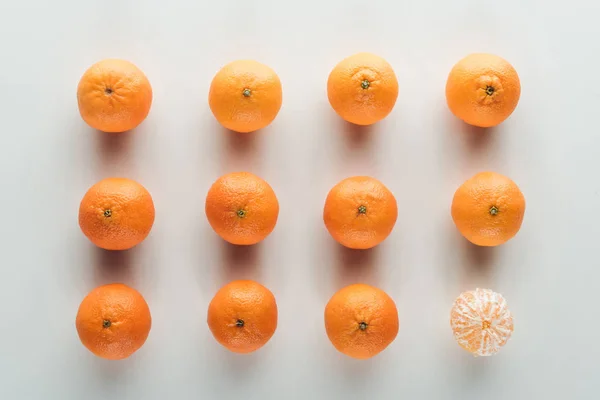 Flat lay with unpeeled tangerines and peeled one on white background — Stock Photo