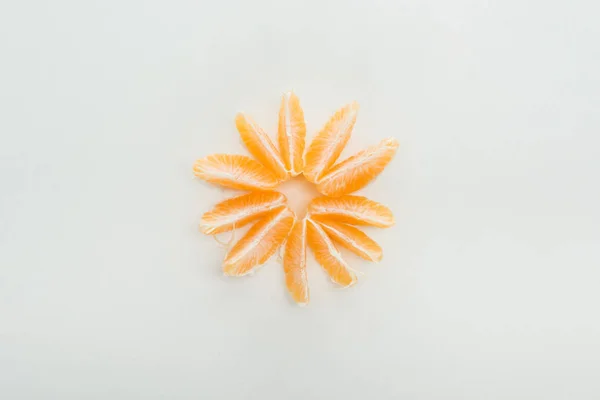 Tendido plano con rodajas de mandarina peladas dispuestas en círculo sobre fondo blanco - foto de stock