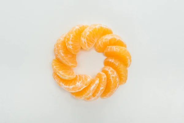 Tendido plano con rodajas de mandarina peladas dispuestas en círculo sobre fondo blanco - foto de stock