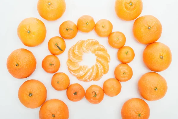 Tendido plano con círculos de rodajas de mandarina peladas y mandarinas enteras sobre fondo blanco - foto de stock