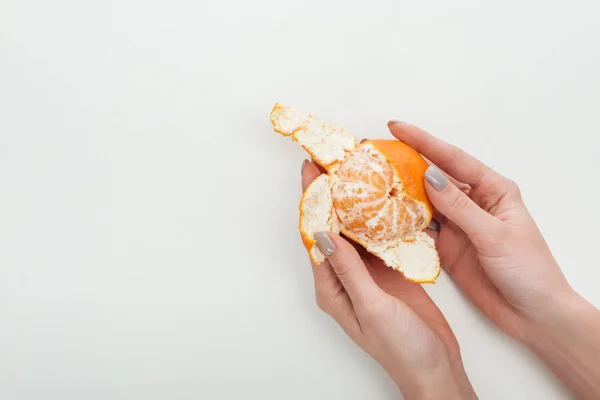 Vista recortada de la mujer pelando mandarina naranja madura sobre fondo blanco - foto de stock