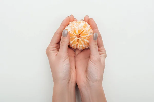 Partial view of woman holding peeled whole tangerine on white background — Stock Photo