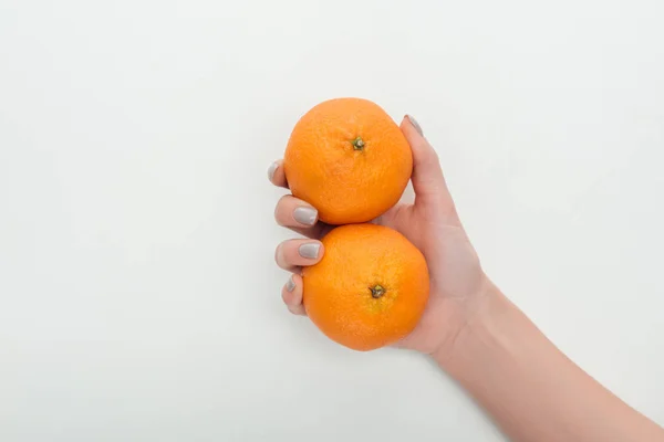 Vista recortada de la mujer sosteniendo dos mandarinas enteras en la mano sobre fondo blanco - foto de stock