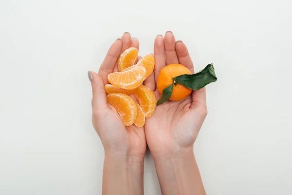 Vue recadrée de la femme tenant des tranches de mandarine pelées et toute la mandarine sur fond blanc — Photo de stock