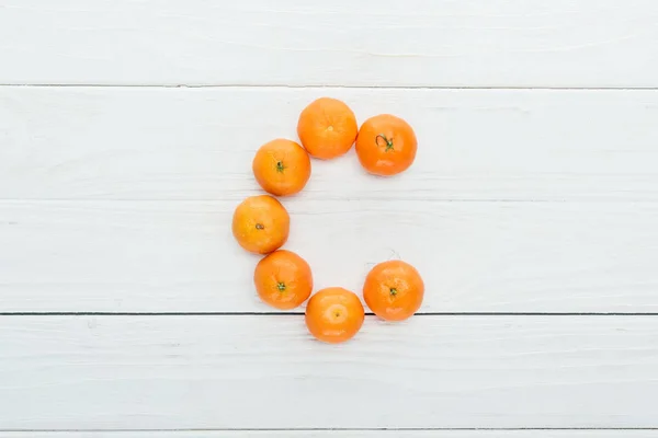 Vista superior de la letra c hecha de mandarinas frescas sobre fondo blanco de madera - foto de stock