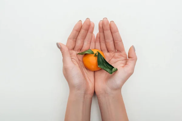 Vue recadrée de la femme tenant la mandarine avec des feuilles vertes dans les mains sur fond blanc — Photo de stock