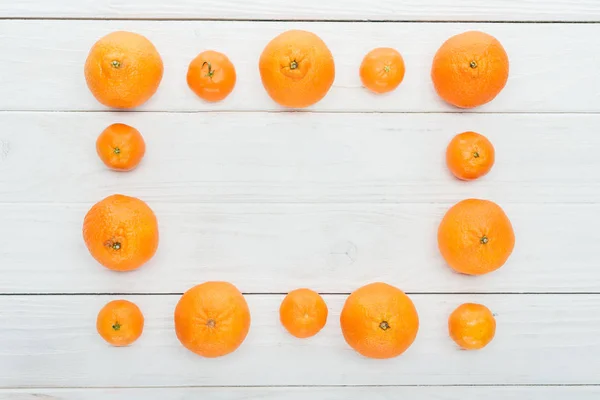 Draufsicht auf quadratischen Rahmen aus reifen orangen Mandarinen auf hölzerner weißer Oberfläche — Stockfoto