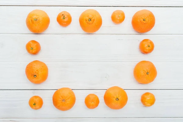 Vista superior del marco cuadrado hecho de mandarinas naranjas maduras en la superficie blanca de madera - foto de stock