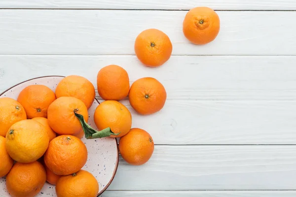 Draufsicht auf reife orange Mandarinen vom Teller auf hölzernem weißem Hintergrund verstreut — Stockfoto