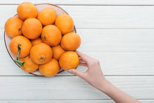 Partial view of female hand near plate with tangerines on wooden white background — Stock Photo