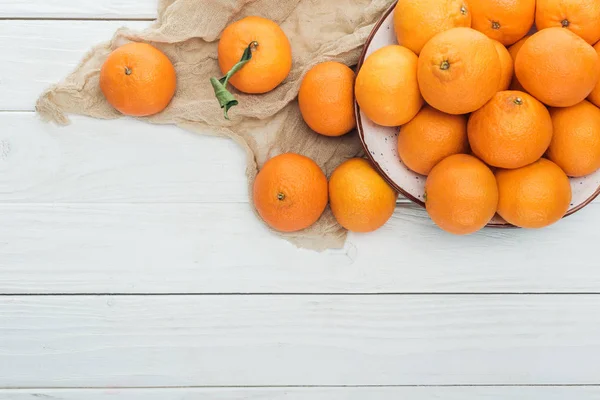 Vue de dessus de mandarines dispersées près de la plaque avec tissu sur fond blanc en bois — Photo de stock