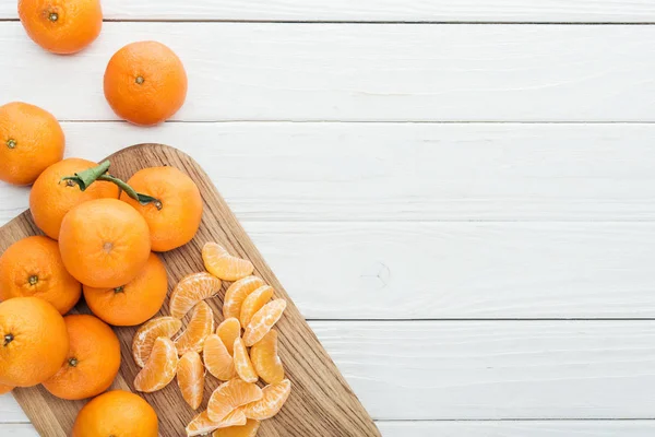 Vue de dessus des tranches de mandarine pelées et des mandarines mûres entières sur une planche à découper en bois — Photo de stock