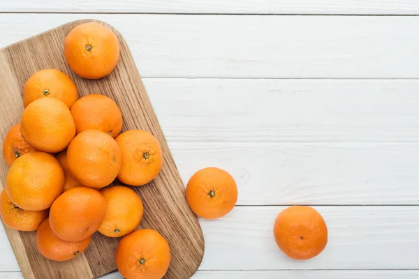 Vue de dessus de mandarines mûres entières éparpillées sur une planche à découper en bois — Photo de stock