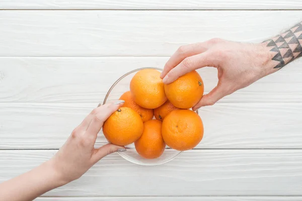 Vista cortada do homem tatuado e mulher tomando tangerinas de tigela de vidro — Fotografia de Stock